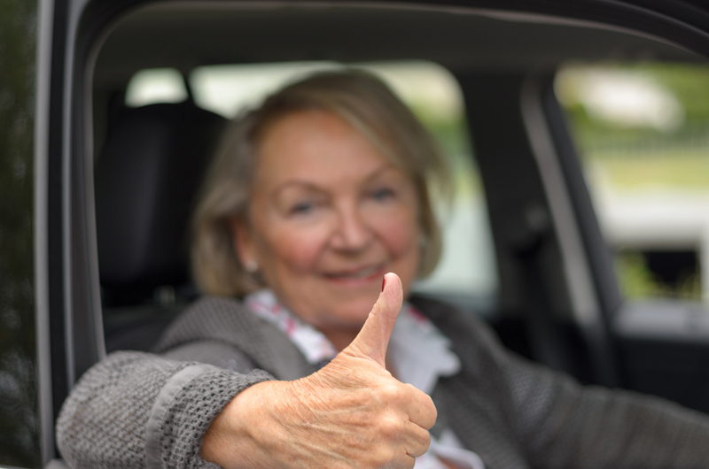 Elderly woman sitting in a car with thumb up while looking to the camera